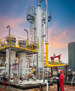 a man in a red suit stands in front of a large industrial plant