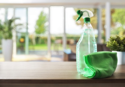 a spray bottle and a green cloth are on a wooden table